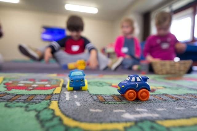 children playing on a rug with cars whilst being cared for by a childminder